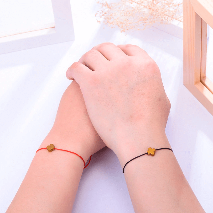 pair of 2 black string bracelets with golden cross charm on a couple's wrists