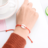 hand wearing a seashell red string bracelet